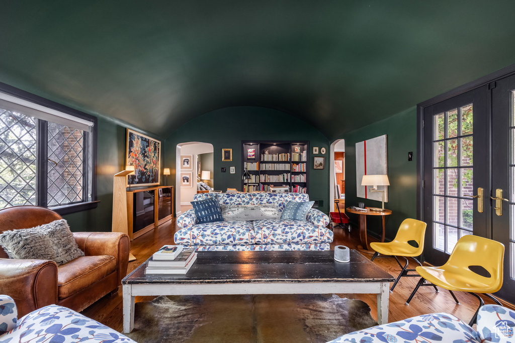 Living room featuring arched walkways, wood finished floors, lofted ceiling, and french doors