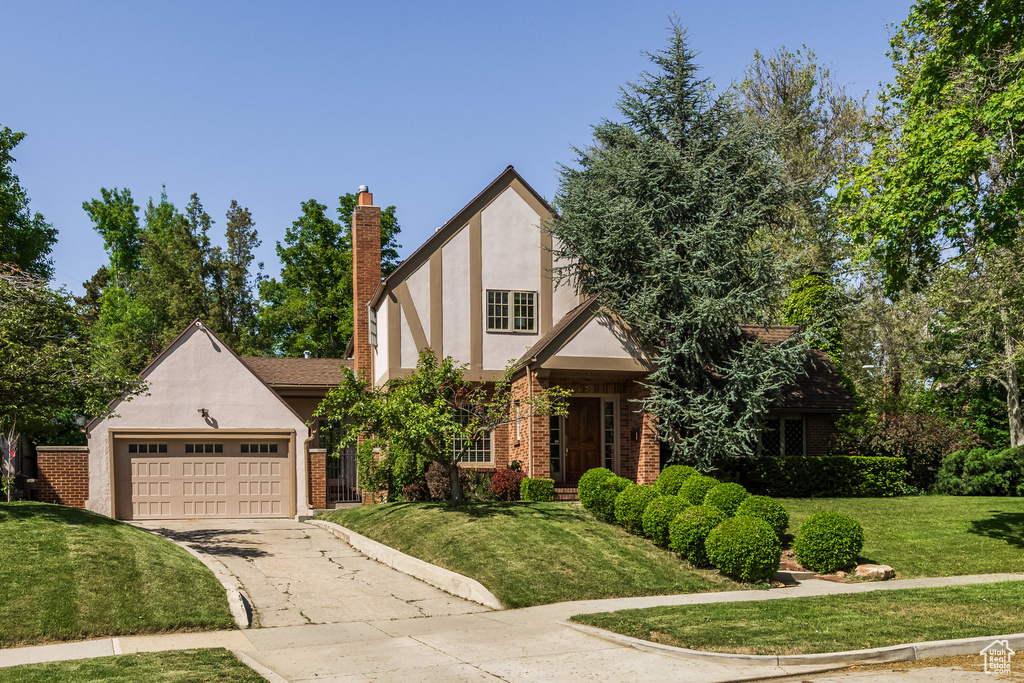 Tudor home featuring driveway, brick siding, a front yard, and stucco siding