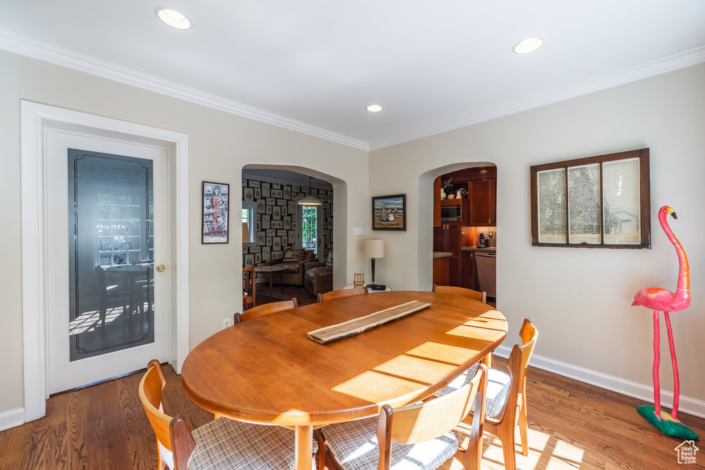 Dining room with arched walkways, light wood-style flooring, recessed lighting, baseboards, and crown molding