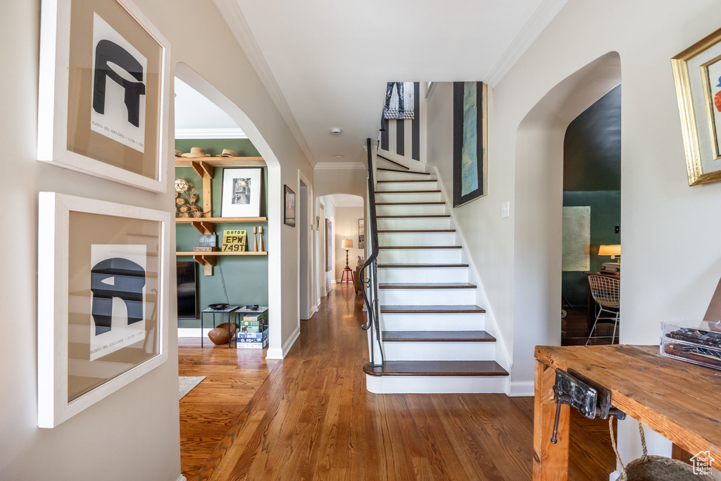 Stairs featuring arched walkways, crown molding, wood finished floors, and baseboards