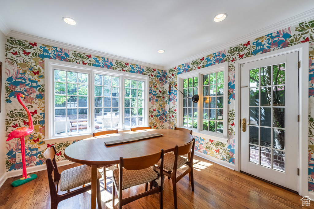 Dining space with wallpapered walls, baseboards, wood finished floors, ornamental molding, and healthy amount of natural light