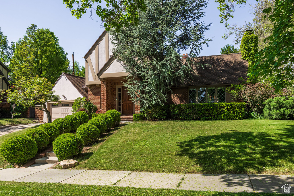 English style home featuring brick siding, a garage, a front lawn, and stucco siding