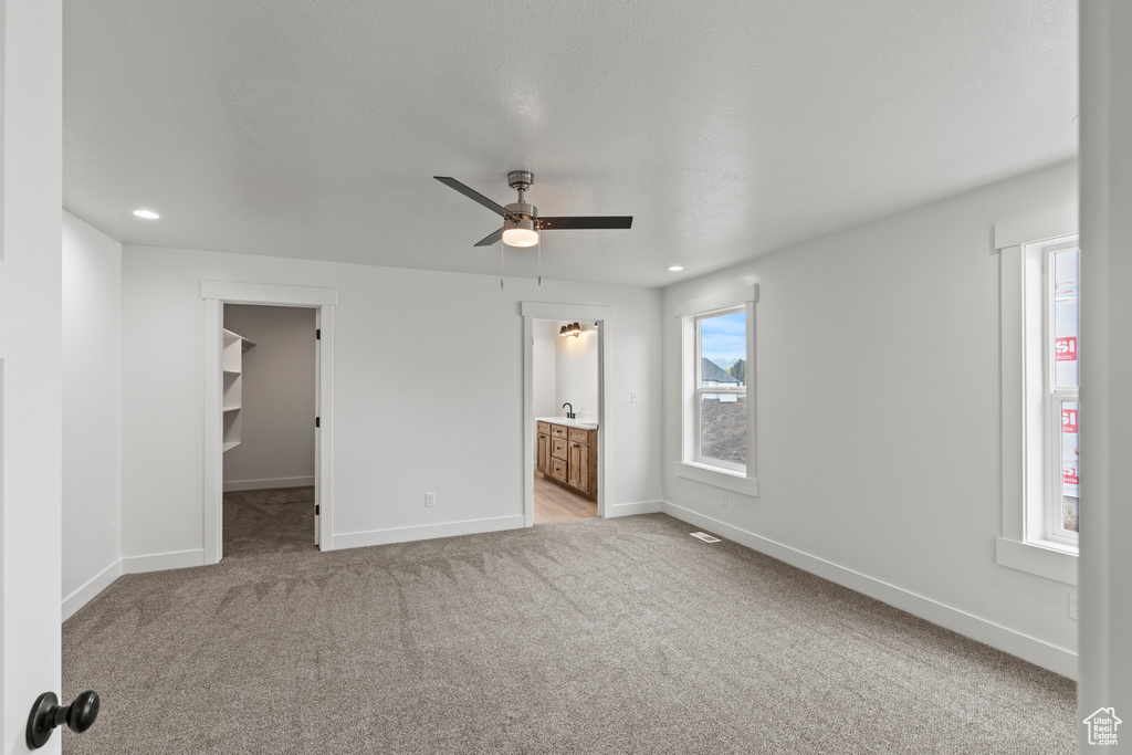 Unfurnished bedroom featuring a spacious closet, baseboards, light carpet, ensuite bath, and recessed lighting
