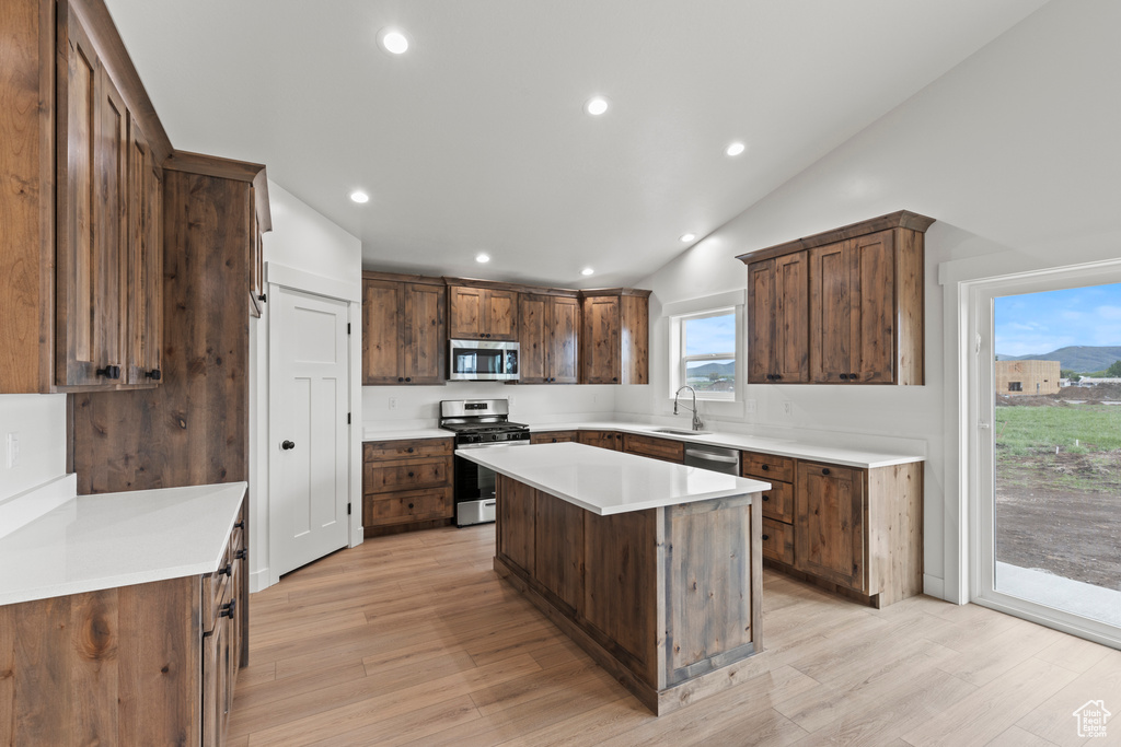 Kitchen with appliances with stainless steel finishes, a center island, light wood finished floors, recessed lighting, and lofted ceiling