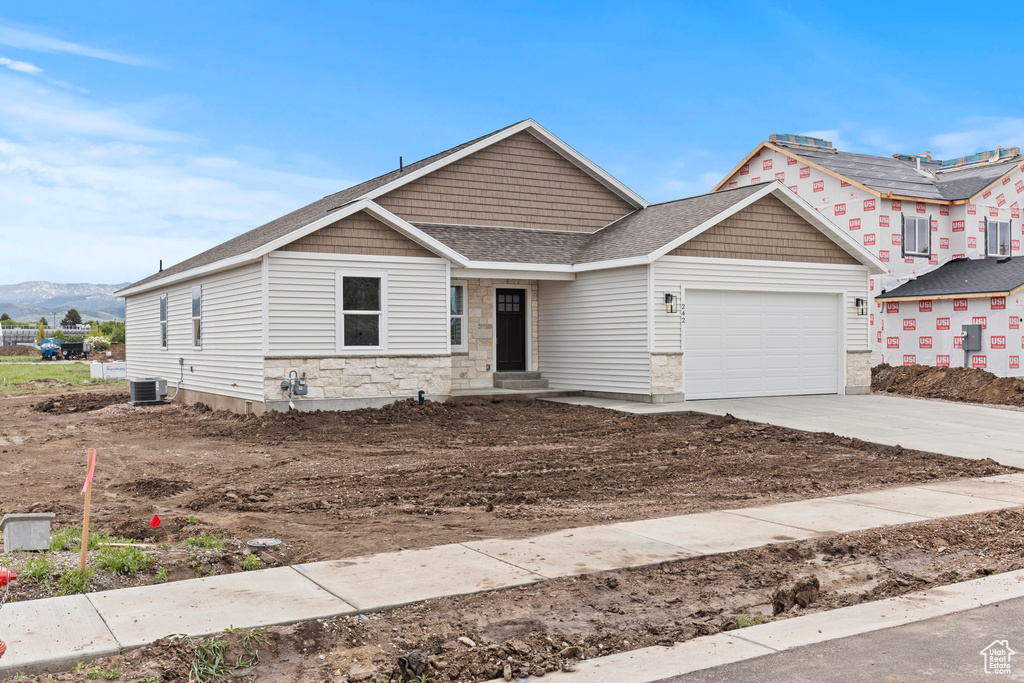 View of front of house featuring central AC unit, a garage, driveway, stone siding, and a shingled roof