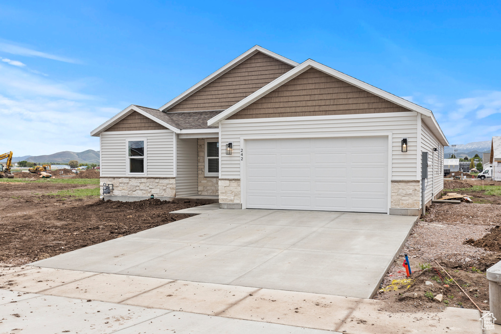 View of front of home featuring stone siding, a mountain view, a garage, and concrete driveway