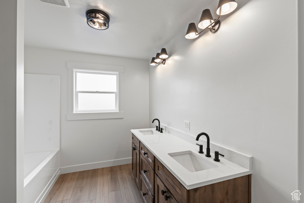 Full bath with wood finished floors, baseboards, double vanity, and a tub