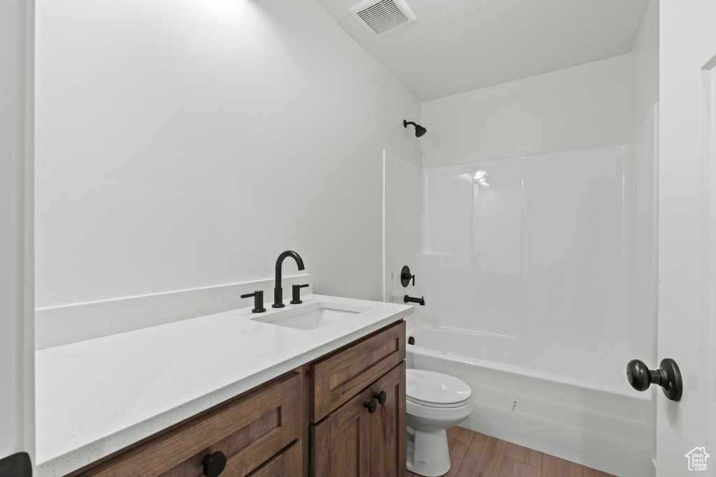 Bathroom with toilet, wood finished floors, vanity, and  shower combination