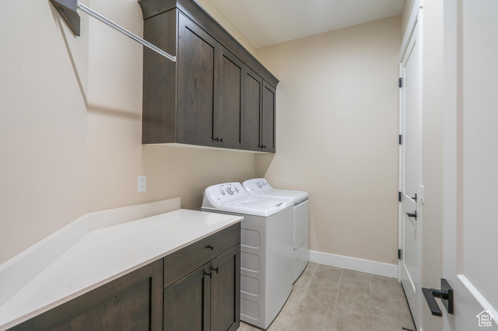 Washroom featuring cabinet space, washing machine and dryer, light tile patterned flooring, and baseboards