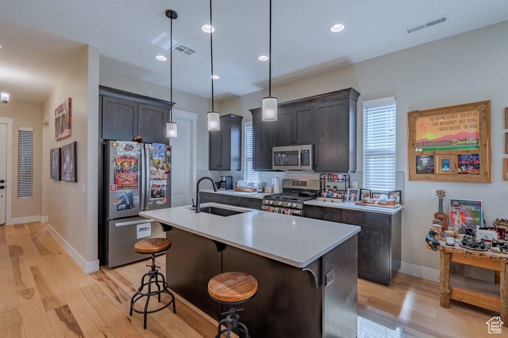 Kitchen with appliances with stainless steel finishes, a sink, light wood-style floors, light countertops, and a kitchen breakfast bar