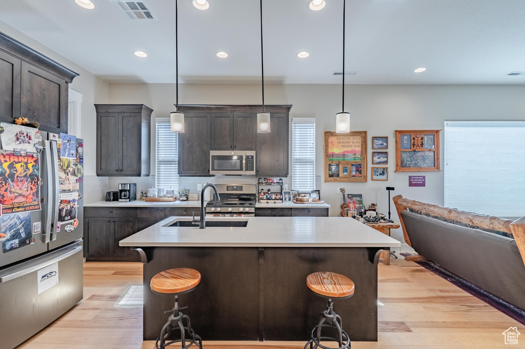 Kitchen with appliances with stainless steel finishes, a sink, light wood-type flooring, light countertops, and recessed lighting