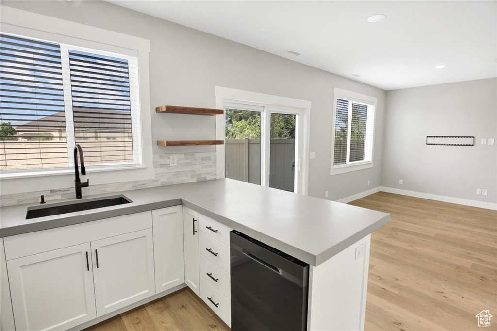 Kitchen with a sink, a peninsula, backsplash, light wood finished floors, and white cabinetry