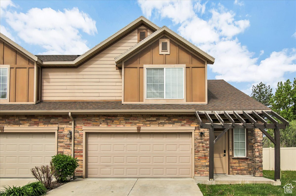 View of property with an attached garage, driveway, stone siding, board and batten siding, and roof with shingles