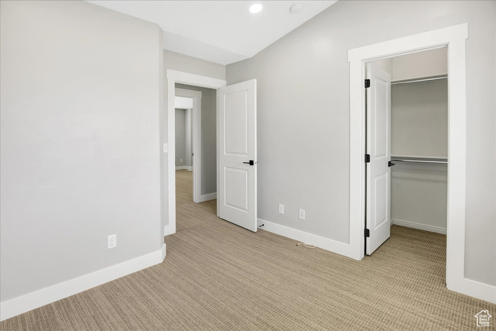 Unfurnished bedroom with light colored carpet, baseboards, a walk in closet, a closet, and recessed lighting