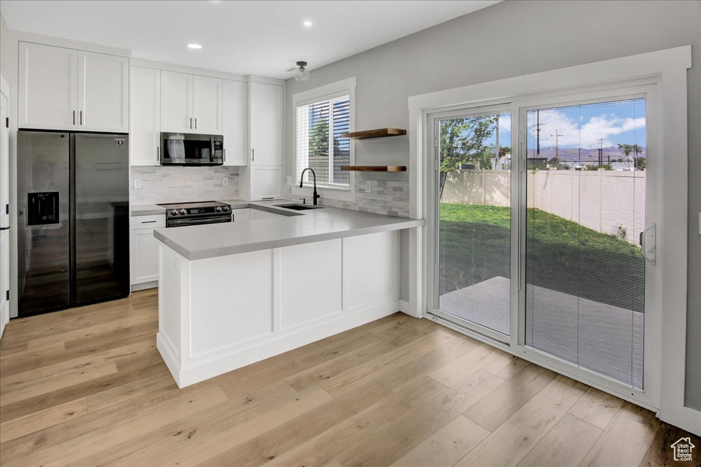 Kitchen with appliances with stainless steel finishes, a sink, recessed lighting, light wood-style flooring, and tasteful backsplash