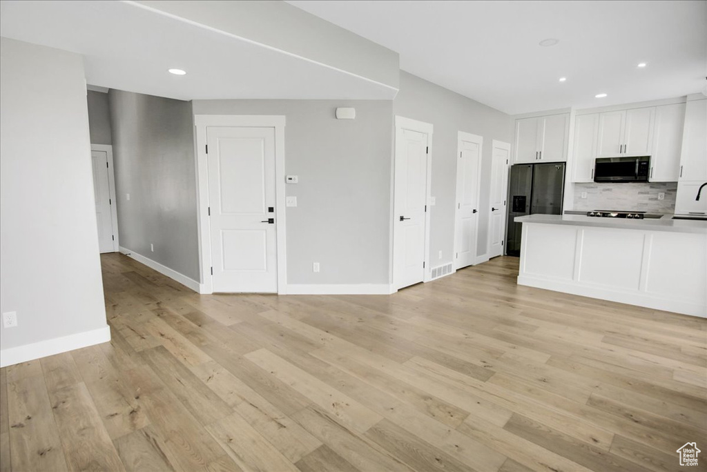 Kitchen with stainless steel microwave, refrigerator with ice dispenser, white cabinets, backsplash, and light wood finished floors