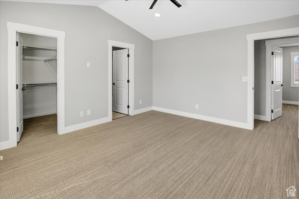 Unfurnished bedroom with a walk in closet, light carpet, lofted ceiling, baseboards, and a closet