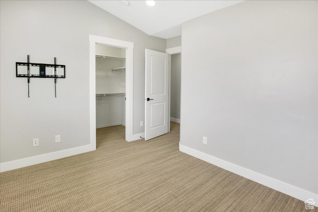 Unfurnished bedroom featuring light colored carpet, a spacious closet, baseboards, a closet, and lofted ceiling
