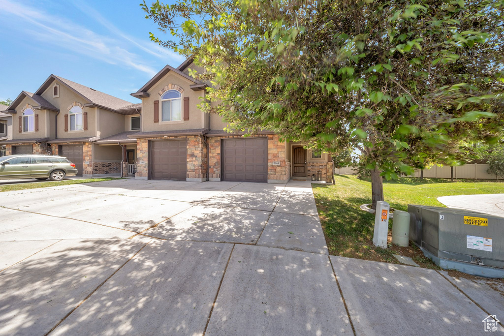 View of front facade with concrete driveway, an attached garage, stone siding, stucco siding, and a front lawn