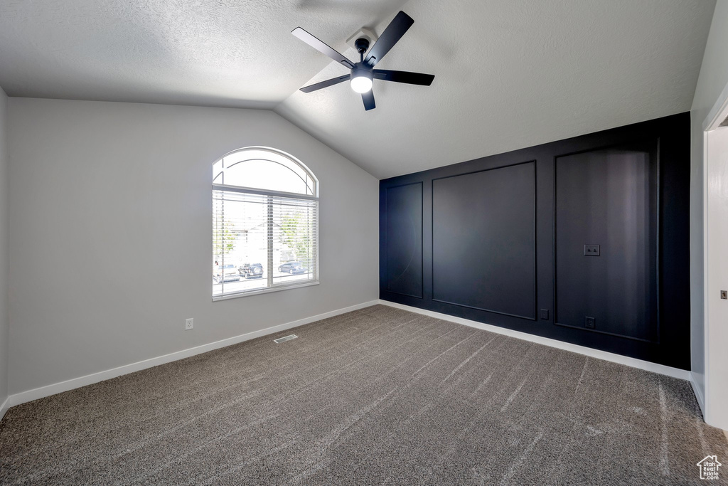 Carpeted empty room with ceiling fan, vaulted ceiling, baseboards, and a textured ceiling