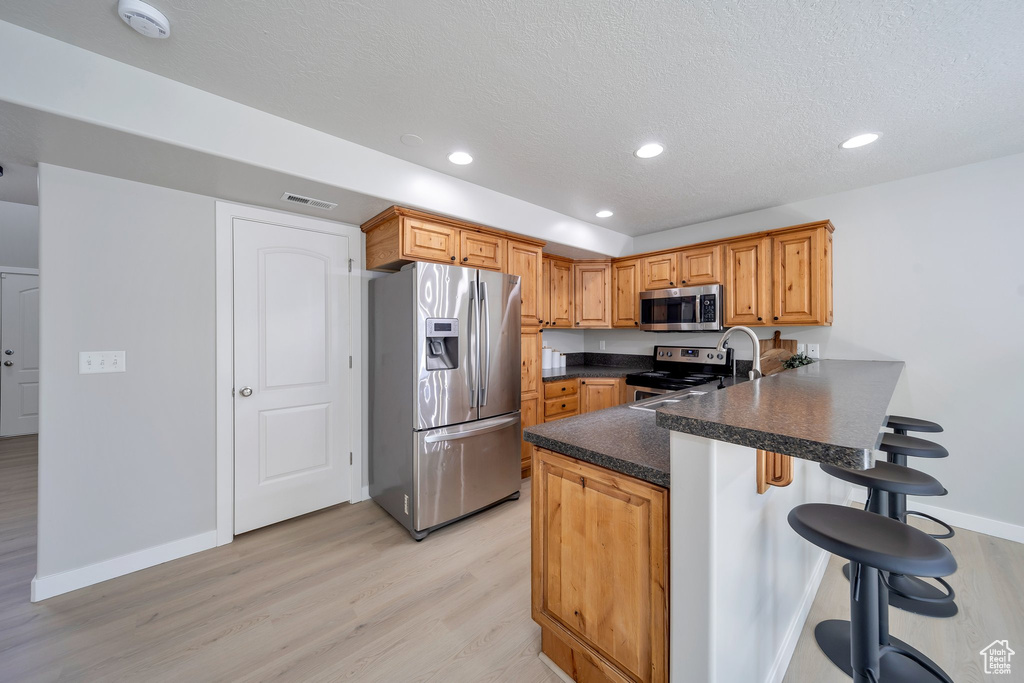 Kitchen with stainless steel appliances, a peninsula, light wood-style flooring, a breakfast bar area, and baseboards