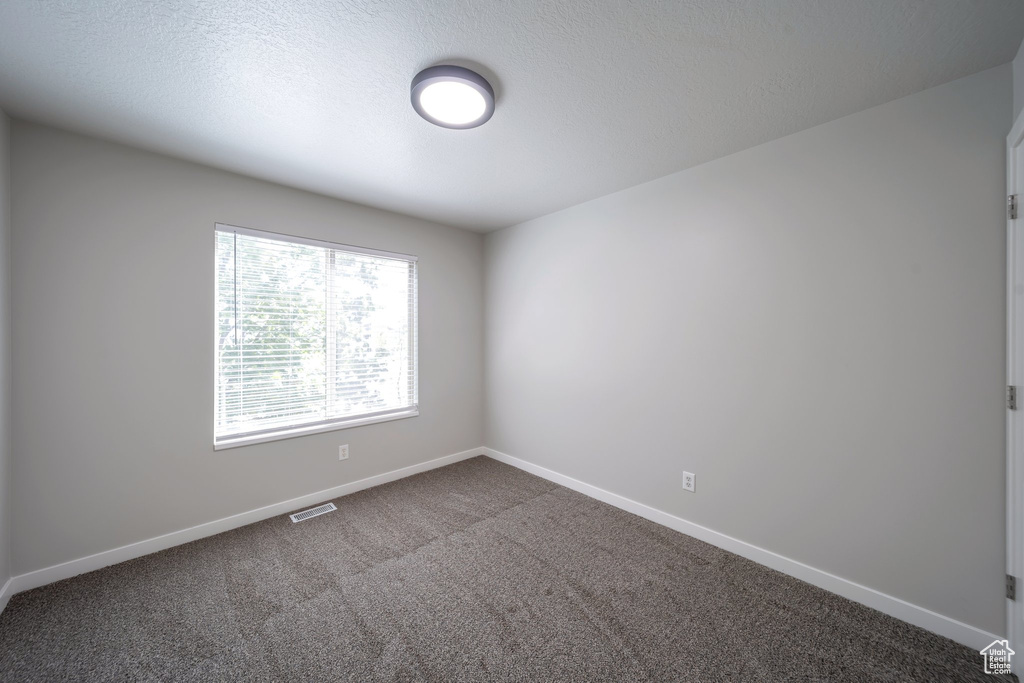 Spare room featuring dark carpet and baseboards