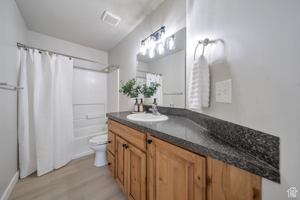 Full bathroom with wood finished floors, toilet, vanity, and shower / tub combo