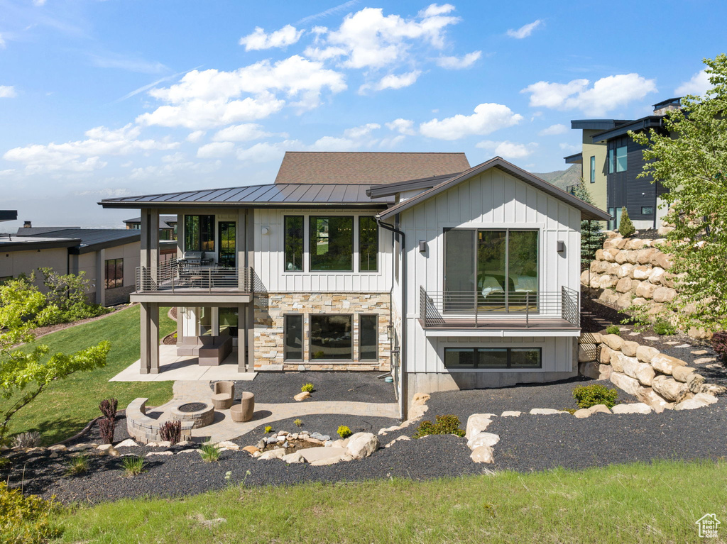 Rear view of house featuring a balcony, a fire pit, a standing seam roof, a patio, and board and batten siding