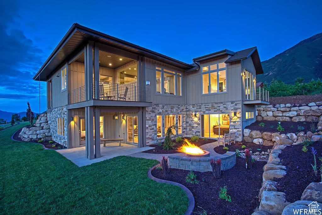Back of property featuring a balcony, stone siding, a patio area, and a yard