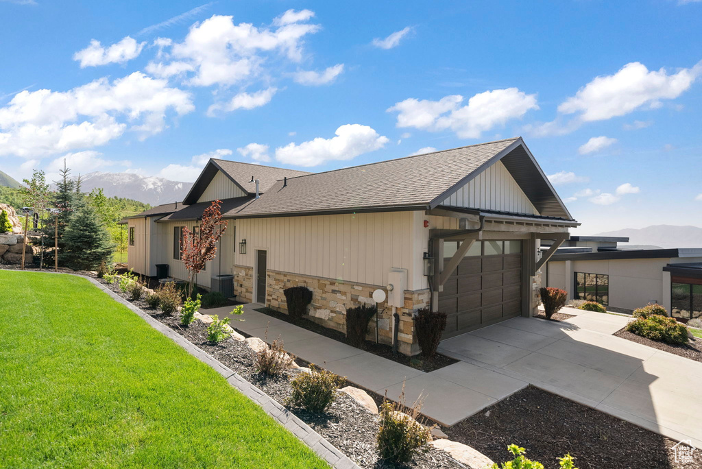 View of property exterior featuring driveway, a garage, stone siding, a mountain view, and a lawn