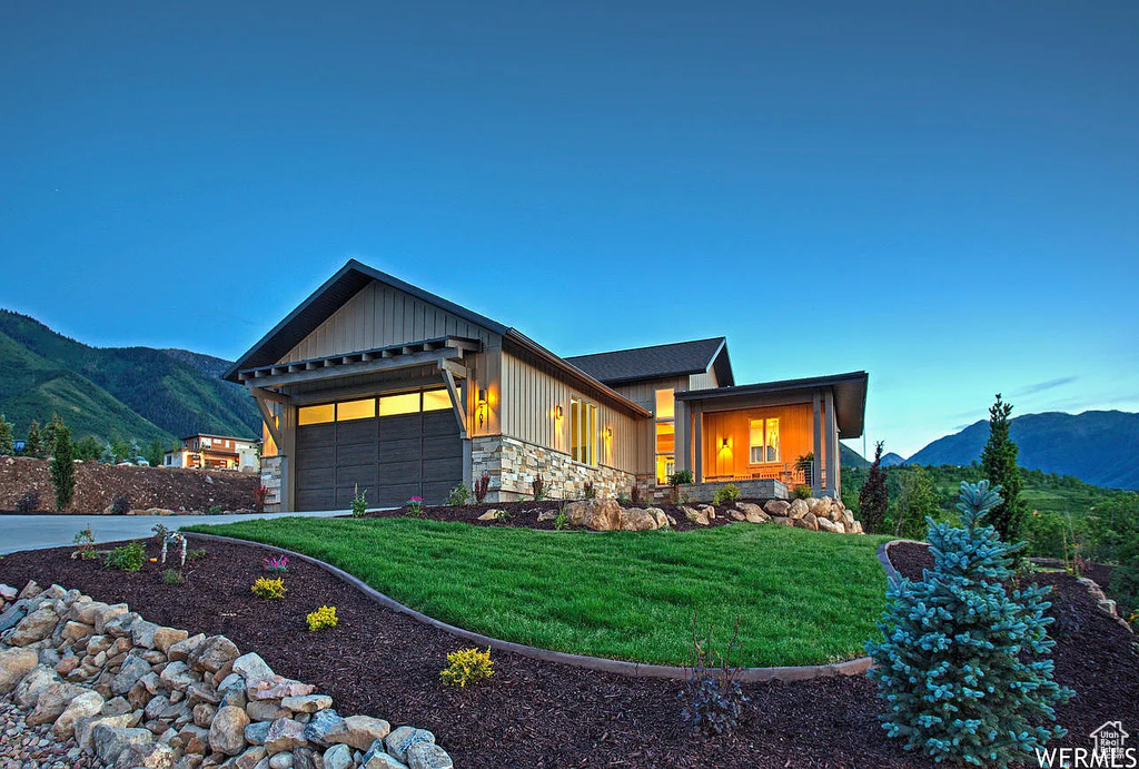View of front of house featuring a mountain view, a garage, a front lawn, and stone siding