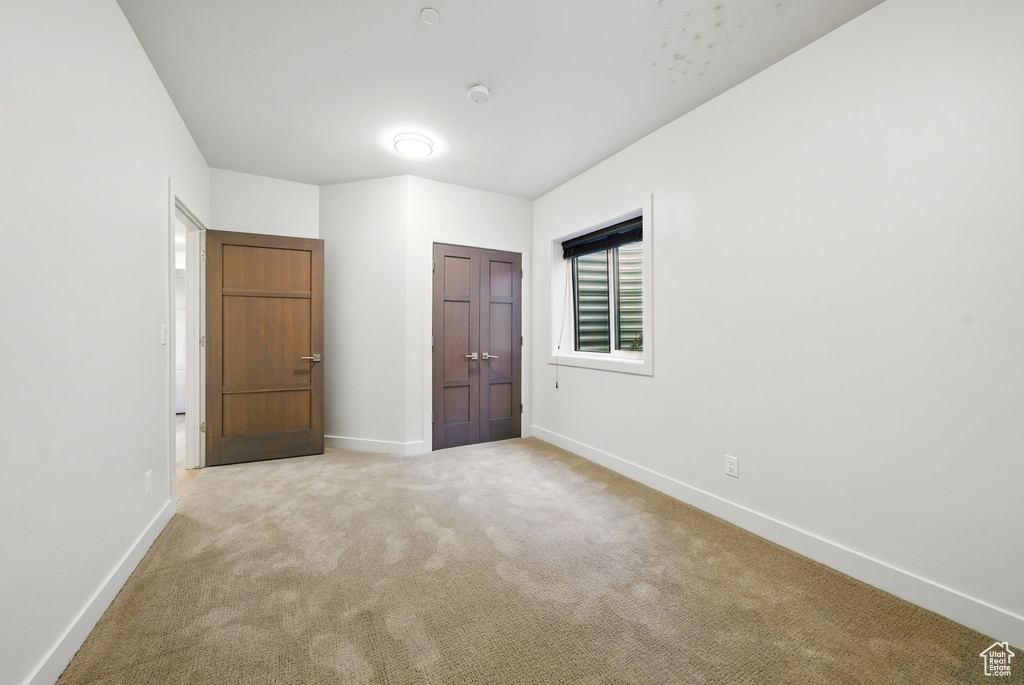 Unfurnished bedroom with light carpet and baseboards