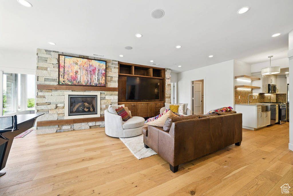 Living room with light wood-style flooring, a stone fireplace, and recessed lighting