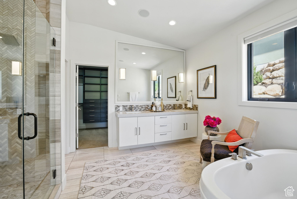 Bathroom featuring a shower stall, a soaking tub, double vanity, recessed lighting, and vaulted ceiling