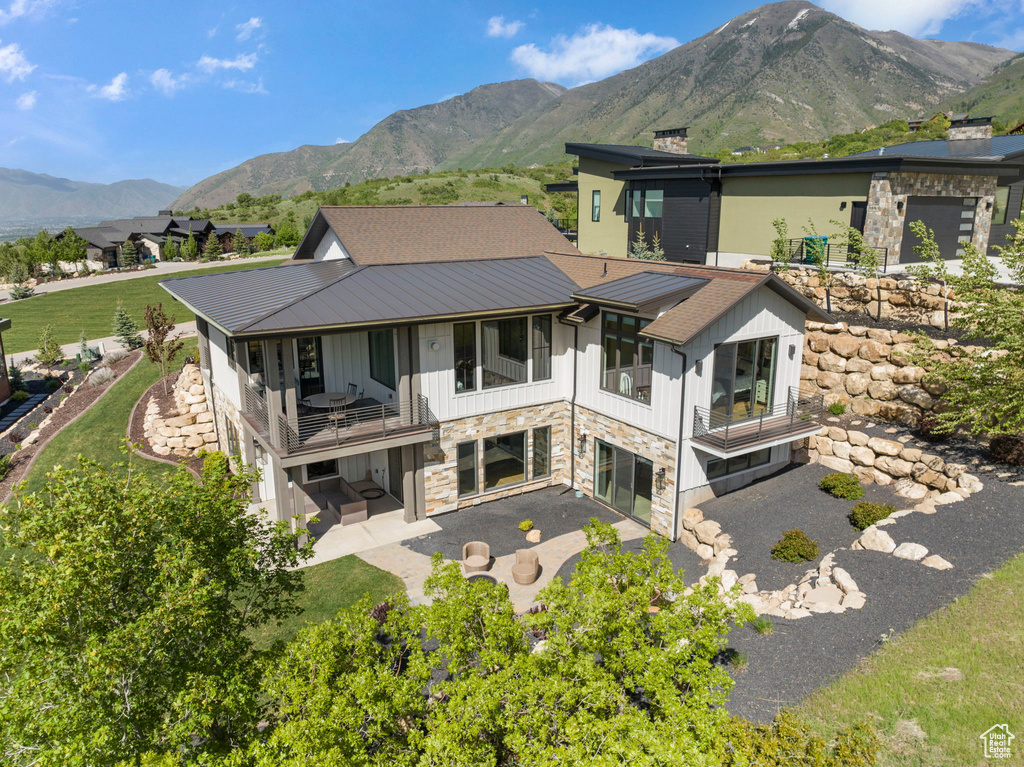 Back of house with a balcony, stone siding, a patio area, and a mountain view