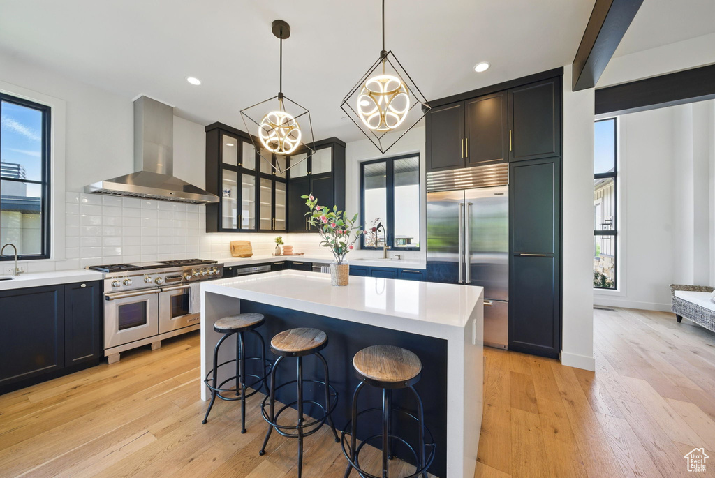 Kitchen featuring high end appliances, wall chimney range hood, plenty of natural light, light countertops, and recessed lighting