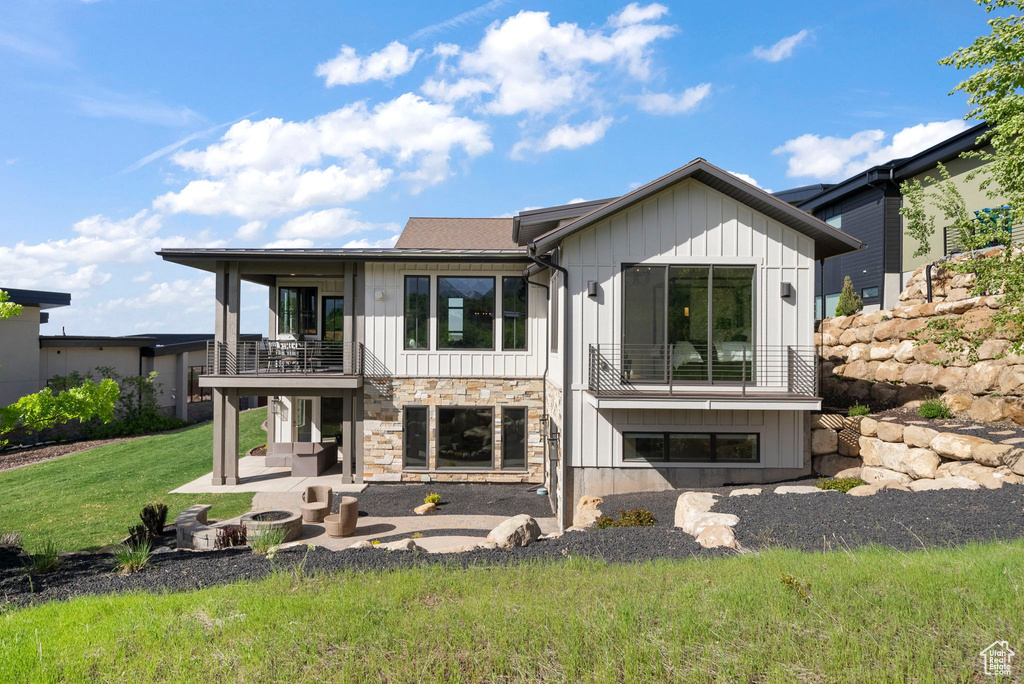 Back of house with a balcony, board and batten siding, a patio area, a yard, and stone siding