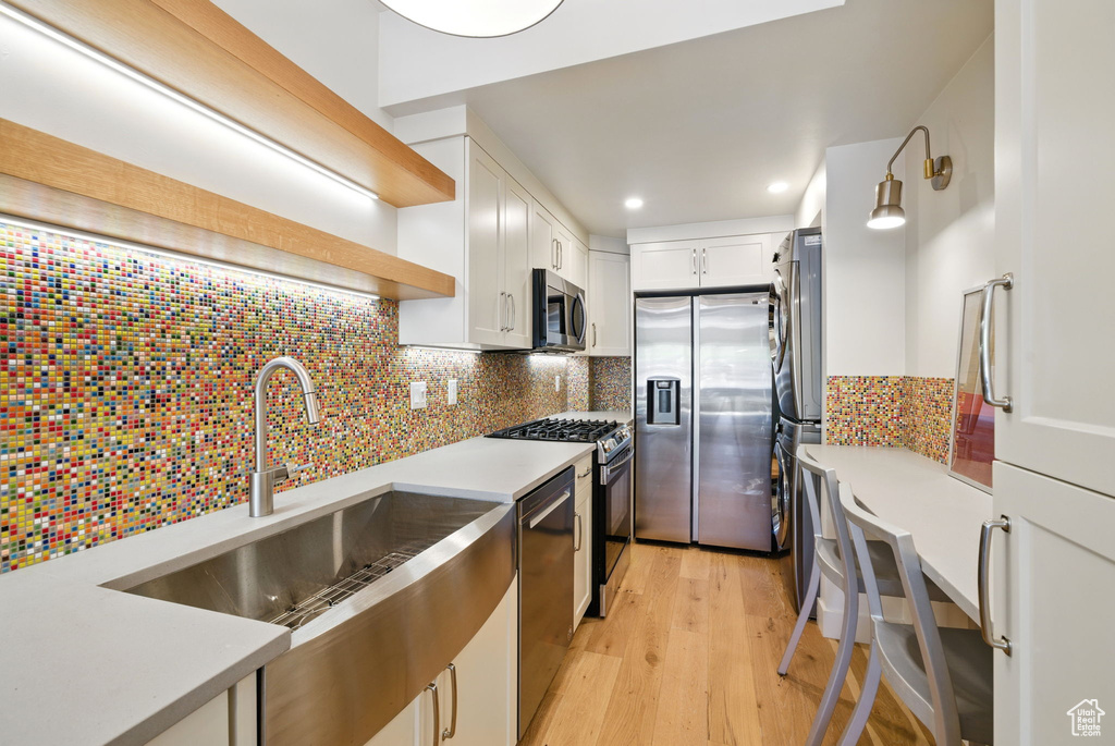 Kitchen with appliances with stainless steel finishes, open shelves, a sink, white cabinetry, and light wood-style flooring