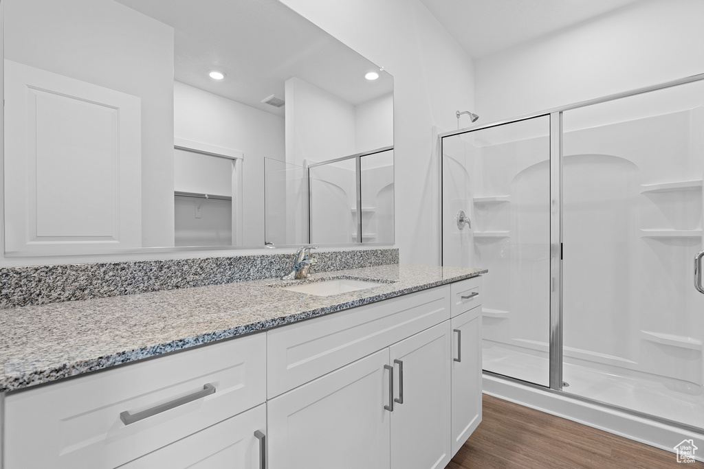 Bathroom featuring a stall shower, vanity, wood finished floors, and recessed lighting