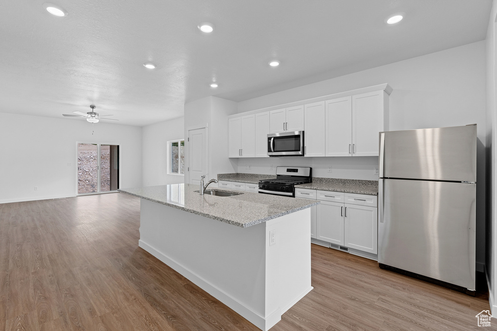 Kitchen featuring appliances with stainless steel finishes, a sink, an island with sink, white cabinets, and recessed lighting
