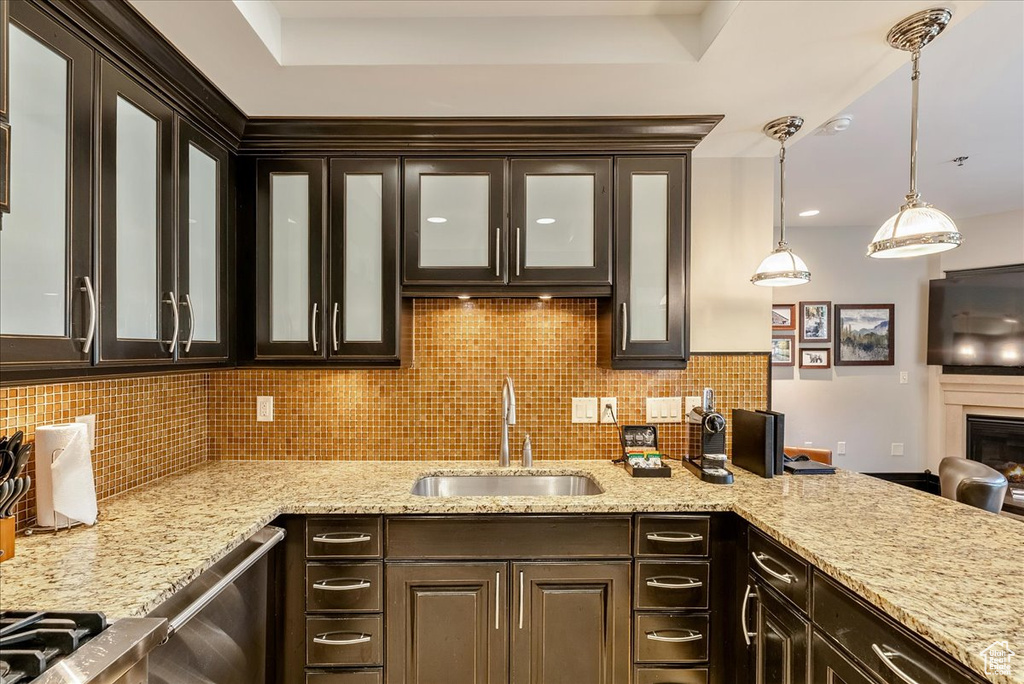 Kitchen with a sink, decorative backsplash, dark brown cabinetry, glass insert cabinets, and pendant lighting