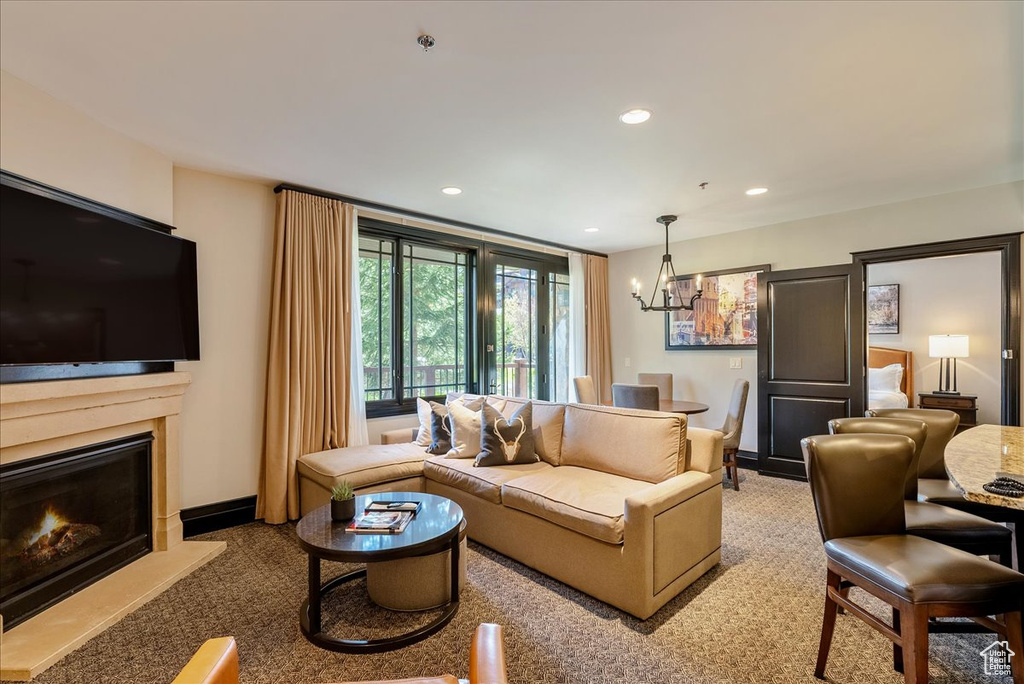 Living area featuring a chandelier, recessed lighting, a warm lit fireplace, baseboards, and carpet flooring
