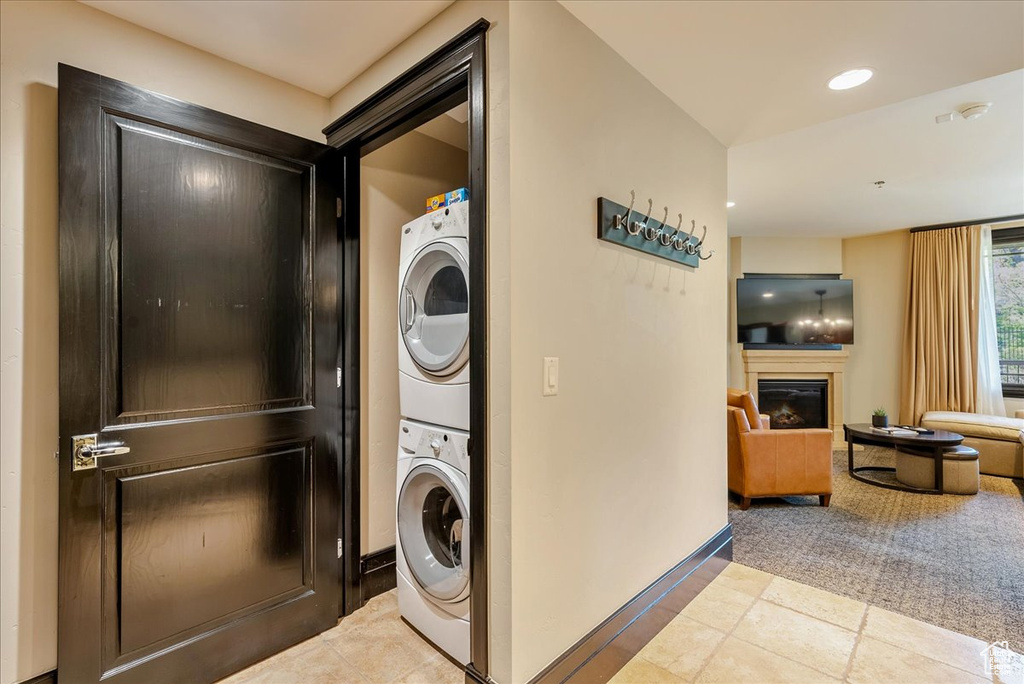 Washroom with stacked washer / drying machine, a glass covered fireplace, baseboards, recessed lighting, and tile patterned flooring