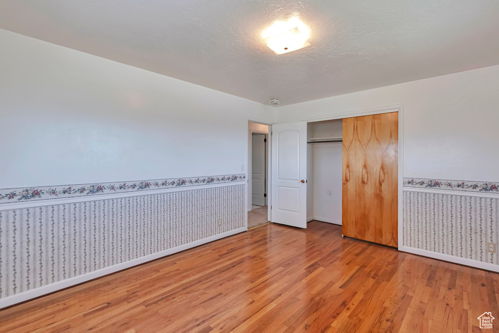 Unfurnished bedroom featuring light wood-style flooring, baseboards, a closet, and wainscoting