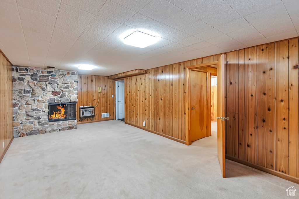 Finished basement featuring carpet floors, a fireplace, wooden walls, heating unit, and baseboards