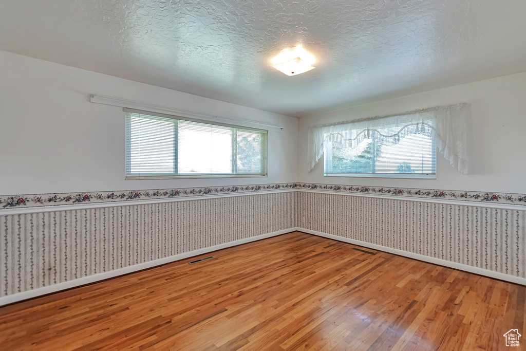 Spare room with wainscoting, light wood finished floors, baseboards, a textured ceiling, and wallpapered walls