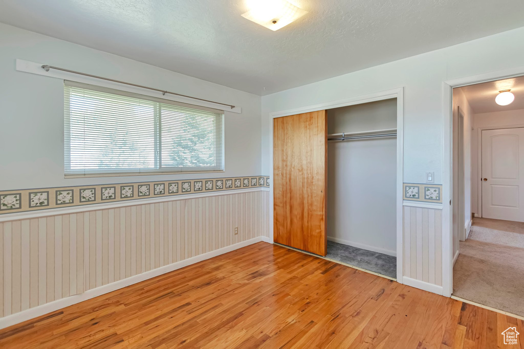 Unfurnished bedroom featuring wood-type flooring, a closet, a wainscoted wall, and baseboards