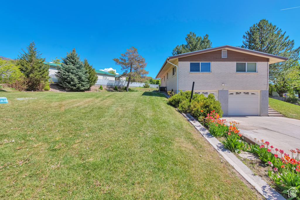 View of property exterior with an attached garage, driveway, a lawn, and central AC unit