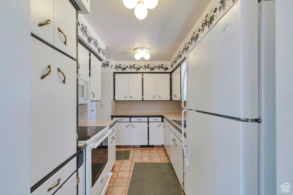 Kitchen featuring white appliances, light tile patterned floors, white cabinets, and light countertops
