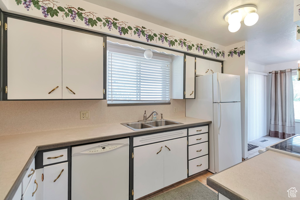 Kitchen with white appliances, a sink, light countertops, and white cabinetry
